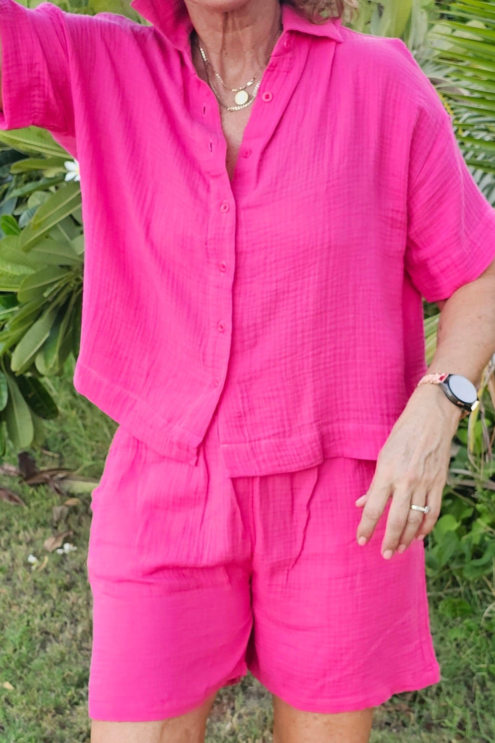 Person wearing a bright pink outfit standing in a natural setting with green foliage.