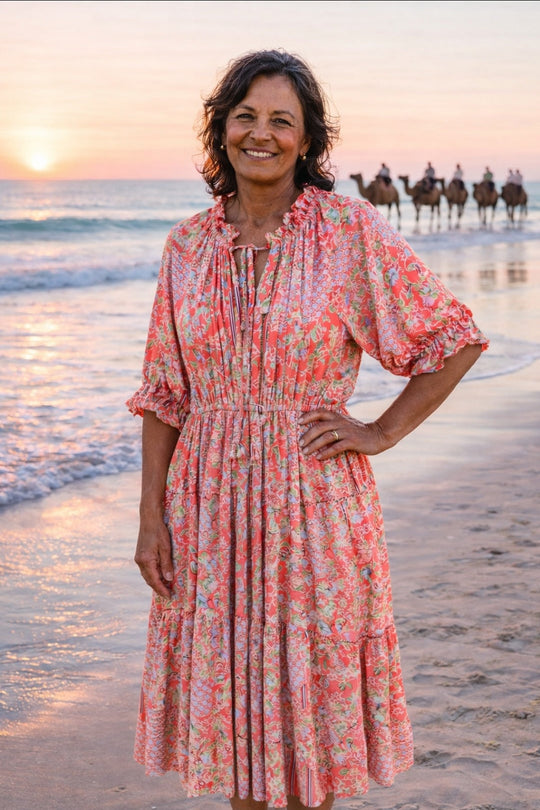 Woman in a floral dress standing on a beach with horses in the background.