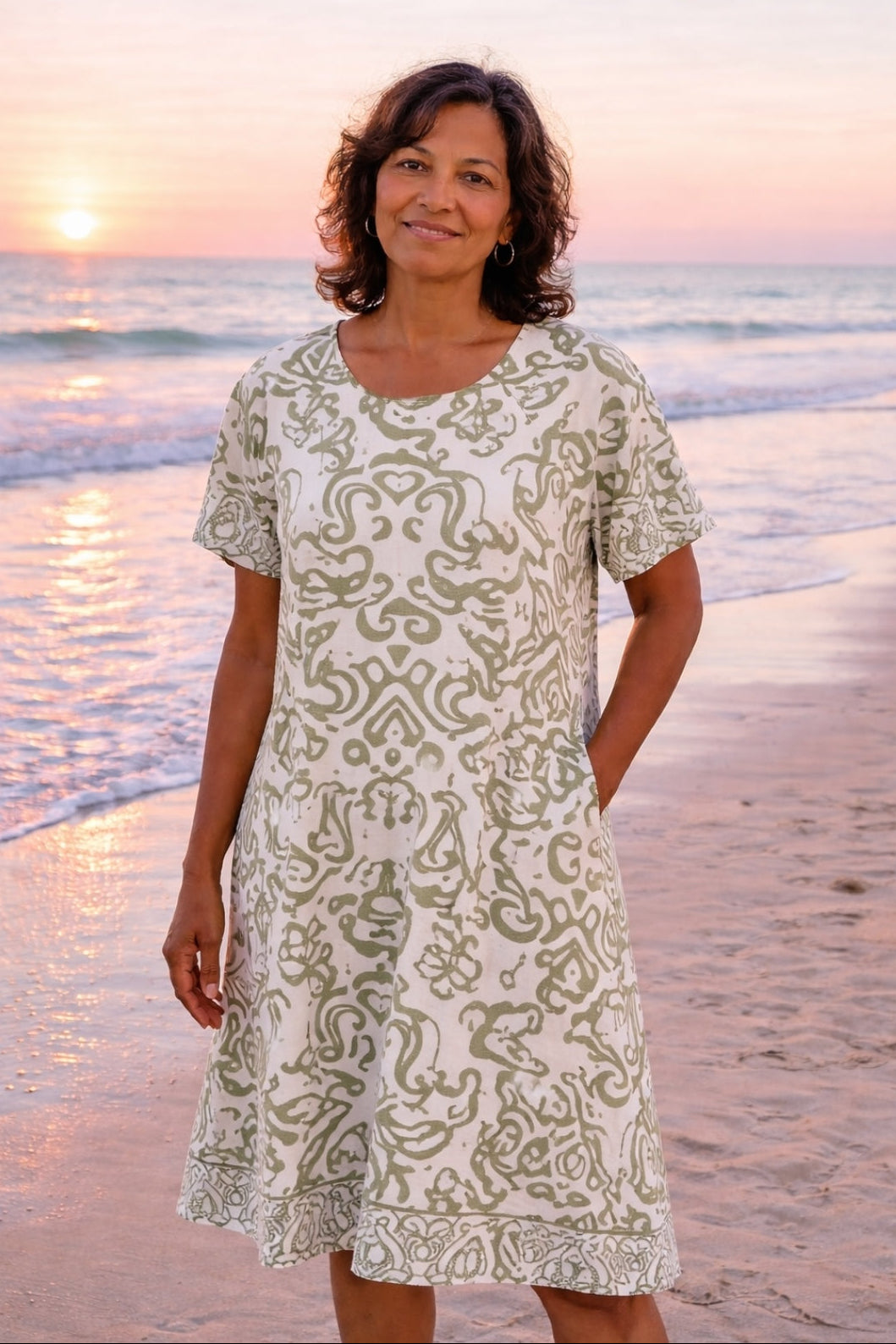 Woman in a patterned dress standing on a beach at sunset