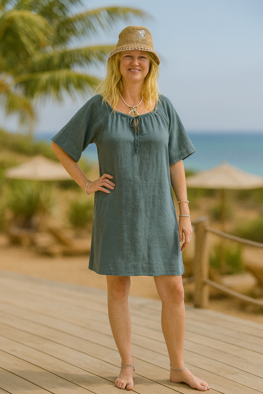 A model wearing the Jill Linen Dress, a casual short sleeve summer dress, posing outdoors near the beach.
