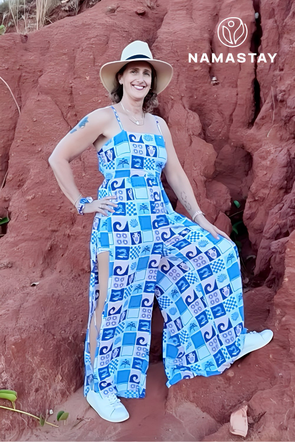 Woman in a blue patterned jumpsuit and hat posing against a red rock wall with 'Namastay' branding.