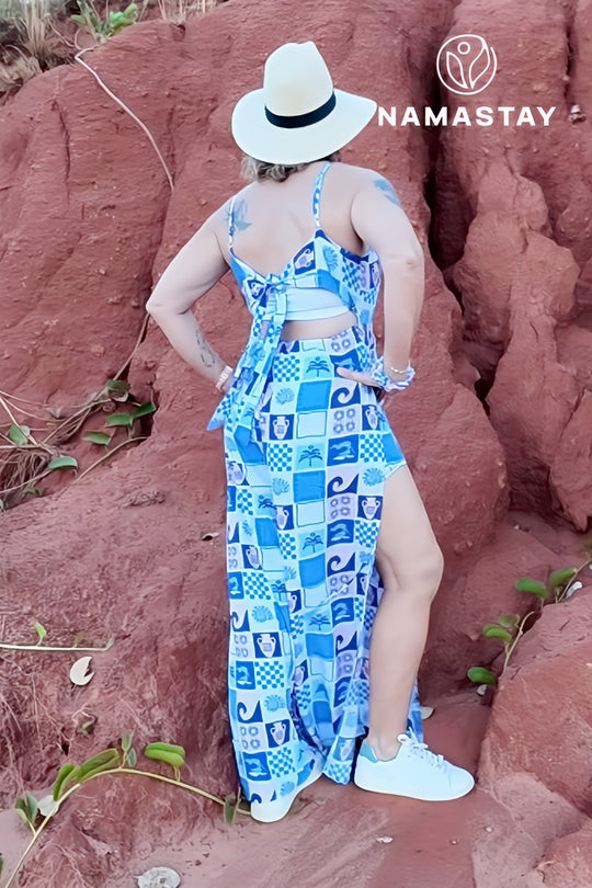 Woman in a blue patterned jumpsuit and white hat standing on red rock terrain with 'Namastay' branding.