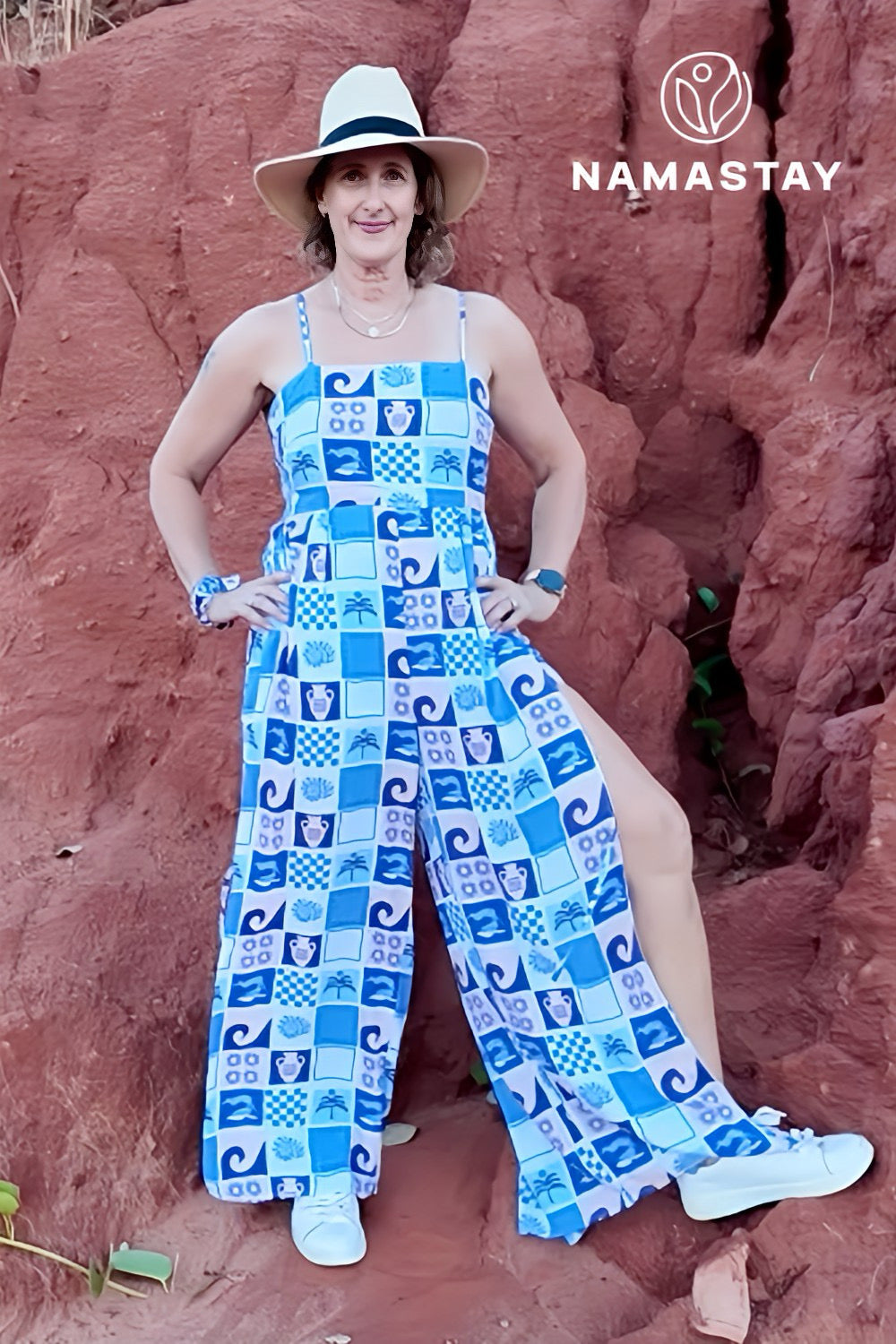 Woman wearing a blue patterned jumpsuit standing against a red rock background with 'Namastay' logo.