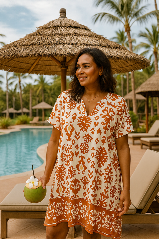 Woman in a boho-inspired women's orange floral dress by the pool with palm trees in the background.